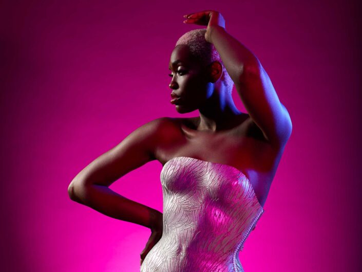 Blondierte afrikanische Frau mit silberner Lederkorsage vor Magentafarbener Wand